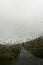 Looking through a car window blurred by raindrops. As a road crosses a bleak moorland valley. On a moody, misty day. Wales, UK