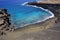 Looking down a cinder cone to Papakolea Beach with people swimming in the ocean and sitting on the sand