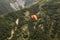 Looking down at a couple hang gliding high over the lower Caucasus mountains with cliffs and trees and a tiny river running far