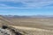 Looking down desert hillside into valley below with barren mountains under a blue sky