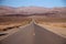 Looking down the middle of a long straight desert road with no one in site for miles in the Death Valley