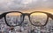 Looking through eyeglasses to city sunset view, focused on lens with blurry background