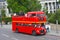 Looking to a typical red London bus for sightseeing with tourists and pedestrians on the walkway