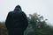 Looking up from behind at a mysterious hooded figure wet from rain on a country path