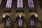 Looking up at six stained glass window on the side of the dimly lit Duke University Chapel\\\'s interior