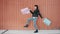Looping of happy woman customer walking outdoors waving shopping bags against wall background