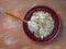 Loose cottage cheese on a shallow brown plate with a wooden spoon with sour cream and seeds, top view