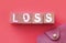 Loss word on wooden blocks with pink wallet besides on warm pink background. Risky investments., debts. or financial loss in