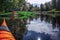 A lot of canoe parked at river shore under the trees at forest edge. Green, black, orange canoes left at rest place. Canoeing