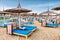 A lot of chaise lounges with blue mattresses on a luxurious beach. Umbrellas for protection from the sun