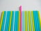 A lot of colorful plastic tubes on a white background. Top view, flat lay. One of them is pink in color and is pushed forward. The