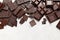 A lot of different dark chocolate pieces and a bar on a light background. View from above.