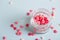 A lot of small candy in form of hearts in open glass jar on light background.