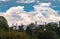 A lot of tops of skyscrapers of Singapore on background, view through jungle, blue sky and big clouds