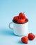 Lots of red ripe fresh strawberries in an enameled white mug on a blue background. There is room for text. Food photo