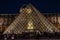 The Louvre Palace and the pyramid by night as entrance inside Louvre Museum, tourists sightseeing, taking pictures