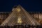 The Louvre Palace and the pyramid by night as entrance inside Louvre Museum, tourists sightseeing, taking pictures