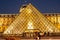 The Louvre Palace and the pyramid by night as entrance inside Louvre Museum, tourists sightseeing, taking pictures