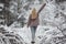 A lovable model girl with long blond hair in a knitted cozy cardigan walks through the winter snowbound forest