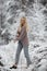 A lovable young woman with long blond hair in a knitted cozy cardigan walks through the winter snowbound forest