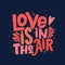 `Love is in the air` lettering isolated on dark blue background. Handwritten poster or greeting card. Valentine`s Day typography.