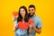 Love is in the air. Romantic arab couple with red paper hearts in hands posing over yellow background, smiling at camera