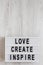 `Love create inspire` words on a lightbox on a white wooden surface, top view. Overhead, from above, flat lay. Copy space