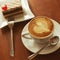 Love cup and art coffee concept. Heart drawing on latte capuccino. Coffee cake with red jelly chocolate biscuit. Daylight.