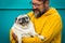 Love dog concept with cheerful adult man hug and hold his own old pug - happy people with animal - colorful yellow and green -