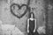 Love hurts. Girl posing with heart graffiti on grey wall