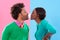 Love, kiss and bubblegum with a black couple in studio on a color wall background for playful romance. Fashion, style or