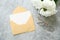 Love letter concept. Envelope with blank white card mockup, bouquet of peonies flowers and glasses on stone background. Romantic