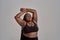 Love my body. Plump, plus size african american woman in sportswear laughing, lifting her arms up in studio over grey