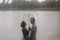 Love story of funny couple walking near river in hard rainfall with umbrella. cute man and woman in white skirt, yellow sweater