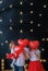 Love and Valentines day. Caucasian family hiding faces behind red heart shaped balloons, black studio background