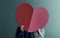 Love and Valentines Day Concept. Young Couple Standing at the Wall and Covered Face by Paper Heart Shape. Bright Color Tone.