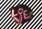 LOVE word handwritten in abstract free style with multicolored paints, black and white striped background.