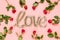 Love word made with shiny shaped golden foil balloon surrounded with red roses on pink background. Mothers, Valentines day,