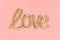 Love word written with shaped golden foil balloon on pink background. Mothers, Valentines day or wedding celebration. Top view,