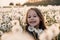 Loveable little brunette lady with dark eyes smiling happily sitting in field of white fluffy dandelions at sunset.