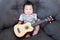 Lovely baby sitting on the soft sofa with mini guitar. babies musician. Practice music skills for children. music and kids.