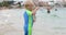 Lovely blond boy is standing in the sea and waving his hand.