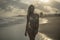 Lovely blonde standing in beautiful pose on black sand beach, pink setting sun