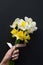 Lovely bouquet of white and yellow narcissus with a pink ribbon in a woman`s hand with a gentle neat blue manicure
