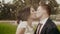 Lovely close-up view of the smiling newlyweds kissing in the rain at the background of the park.