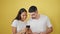 Lovely couple, caught in a beautiful moment, confidently smiling while typing on smartphones, against an isolated yellow