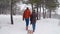 Lovely couple walking pulling sled on snowy winter day. Man with girlfriend go sledding on snowfall. Woman going to