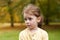 Lovely cute red-haired little girl in the autumn park outdoors. Lovely baby in front of falling leaves