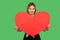 Lovely cute woman holding huge red heart and looking at camera with toothy smile, showing symbol of love and charity