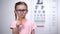 Lovely girl in glasses chewing carrot, vitamin A for good vision, healthcare